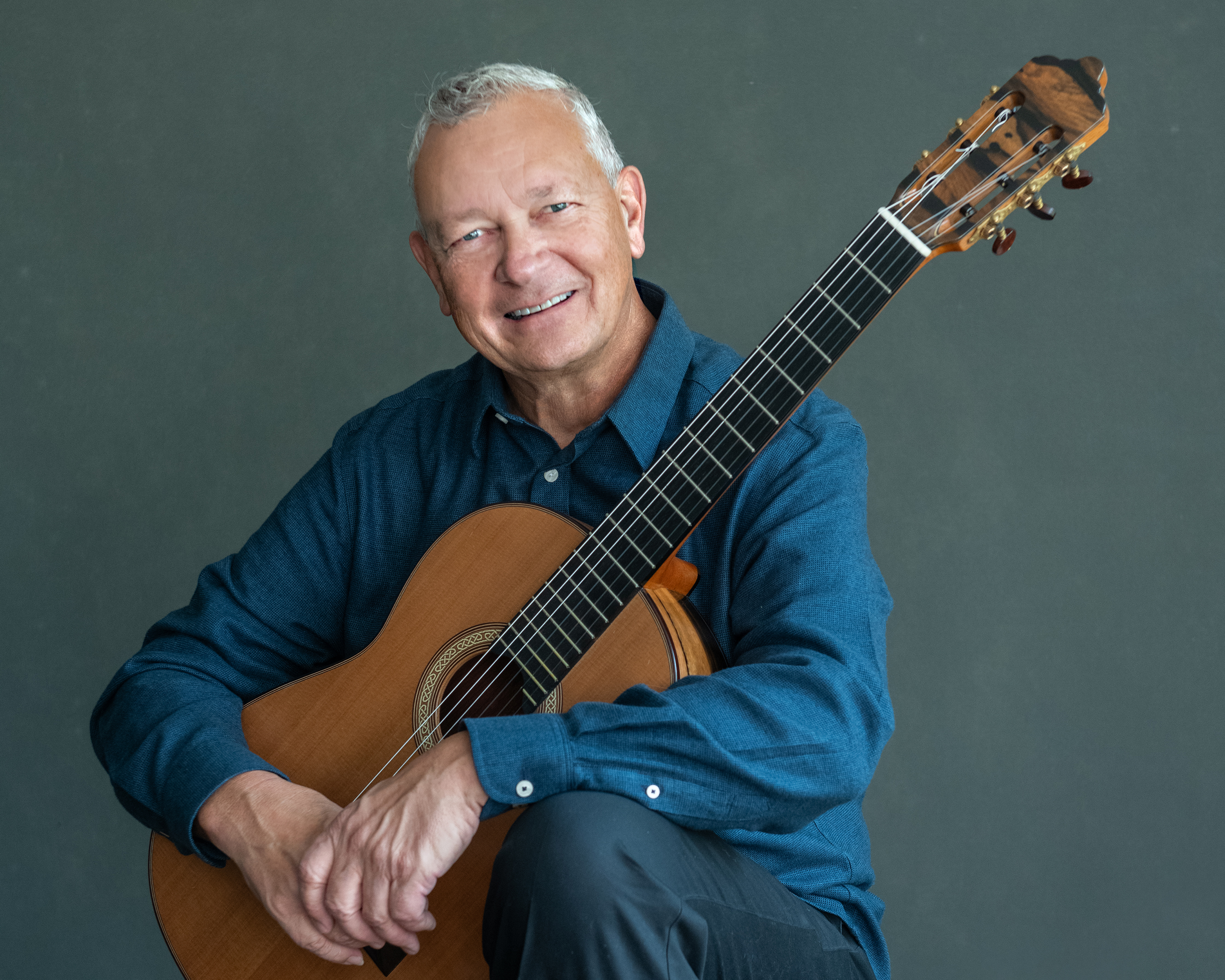 Christopher Laughlin sits with his guitar smiling at the camera.